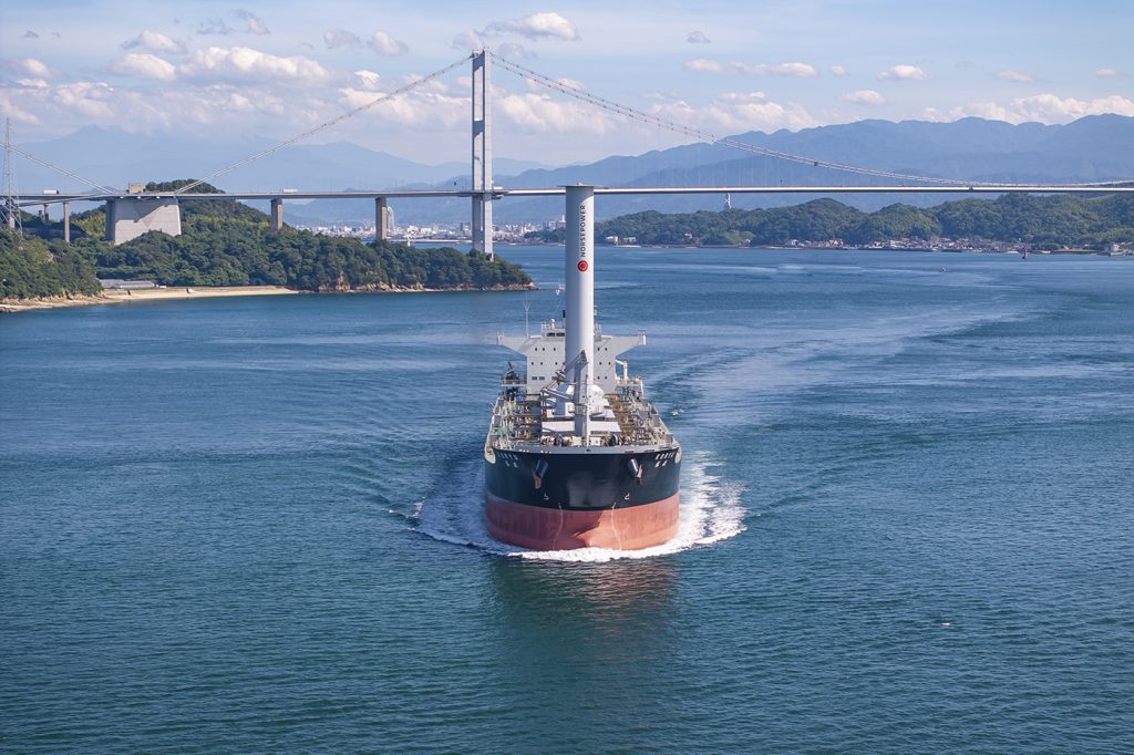 a ship showing a large rotor sail travelling through a bay